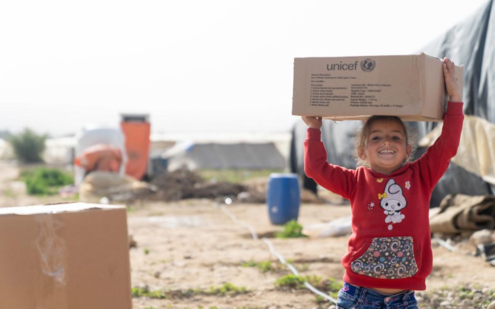 Jordanien: Ein Mädchen trägt ein Paket mit Hilfsgütern und lacht