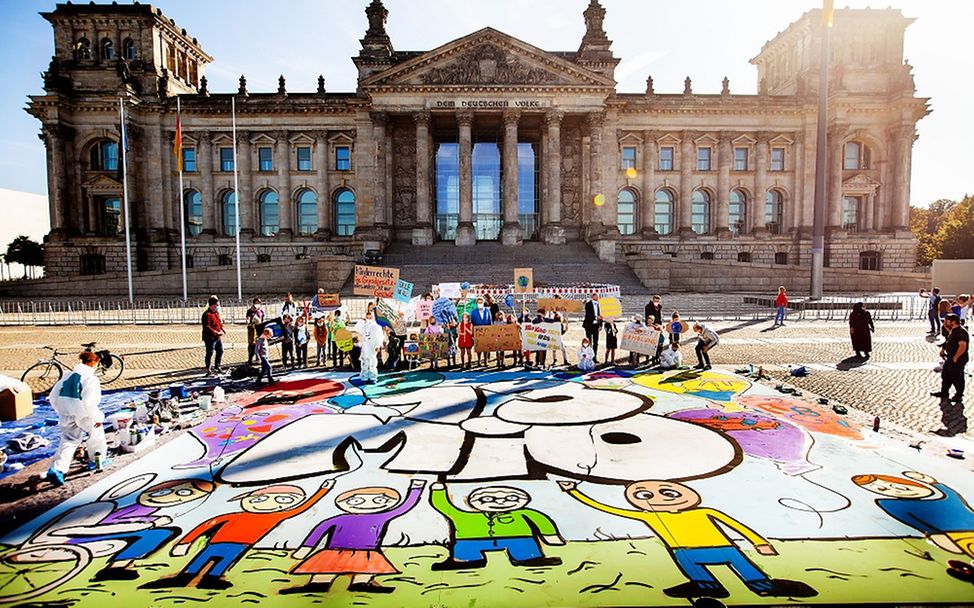 Eine große Gruppe von Kindern und Jugendlichen präsentierenvor dem Berliner Reichstag ihr Bodengemälde.