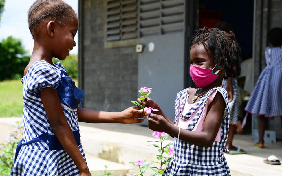 Elfenbeinküste: Zwei Mädchen mit Maske reichen sich eine Blume