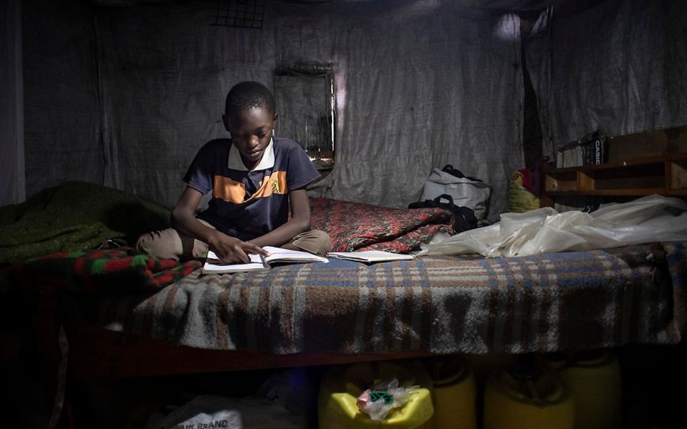 Kenia: Junge sitzt über einem Schulbuch, da er nicht am Online-Unterricht teilnehmen kann.