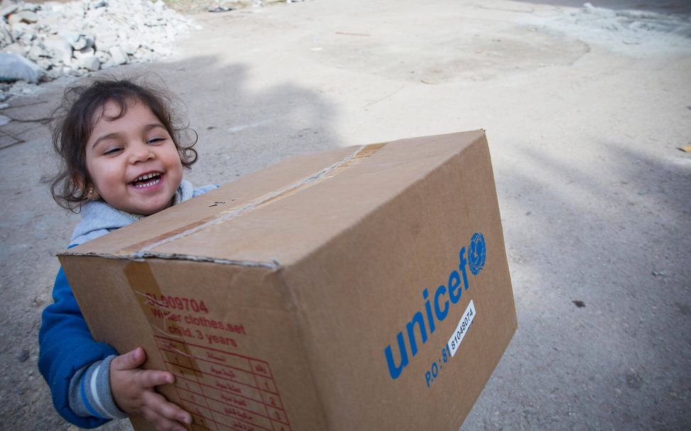 Last Minute Geschenke zum Muttertag: Ein syrisches Mädchen trägt ein Paket mit Winterkleidung