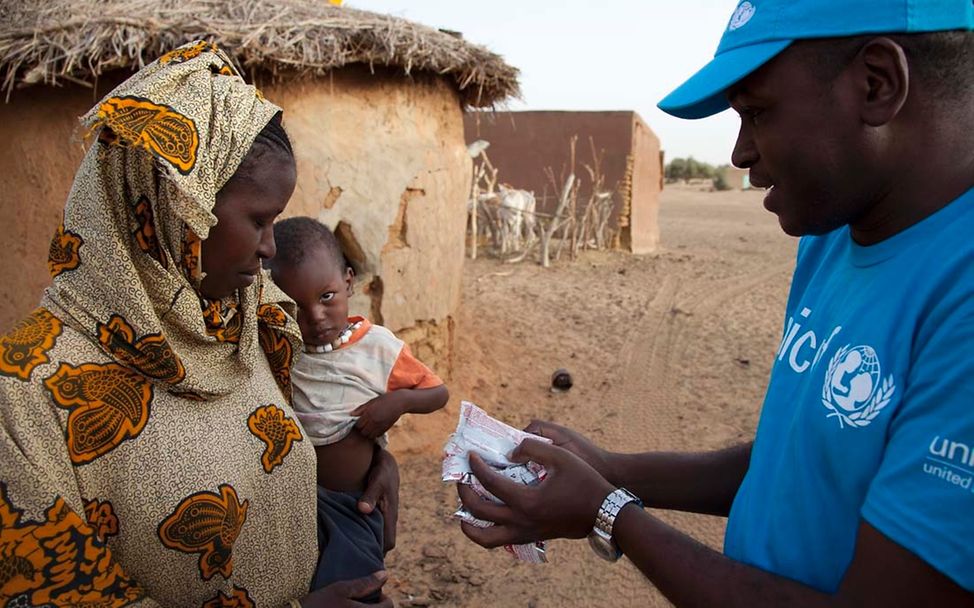 Ein UNICEF-Helfer übergibt einer Mutter mehrere Päckchen Erdnusspaste für ihr mangelernährtes Kind.