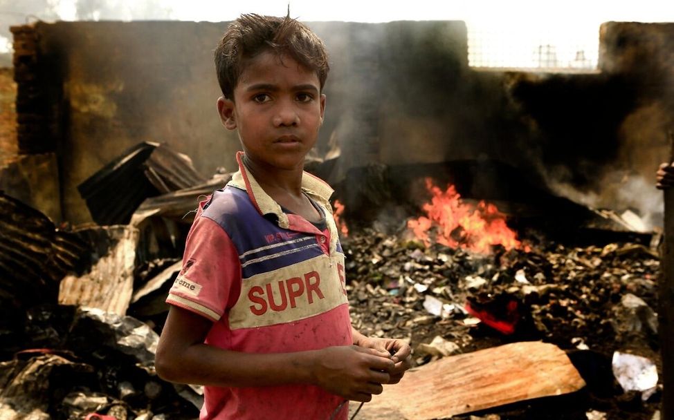 Ein Junge steht nach dem Feuer im Flüchtlingscamp vor den immer noch brennenden Überresten des provisorischen Lagers.