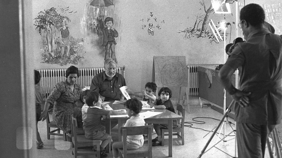 Ustinov sitzt mit Kindern an einem Tisch.