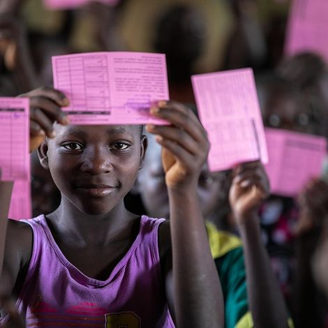 Afrikanische Schulkinder halten stolz lächelnd ihre Impfausweise in die Höhe. 