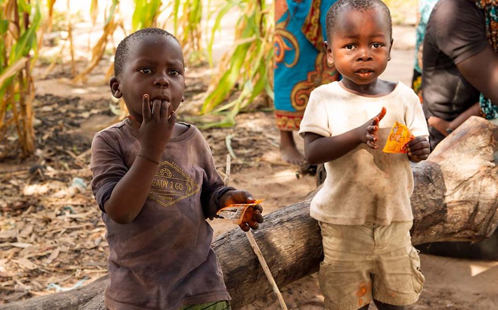 Mosambik: Zwei Jungen stehen vor einem auf dem Boden liegenden Baumstamm. 