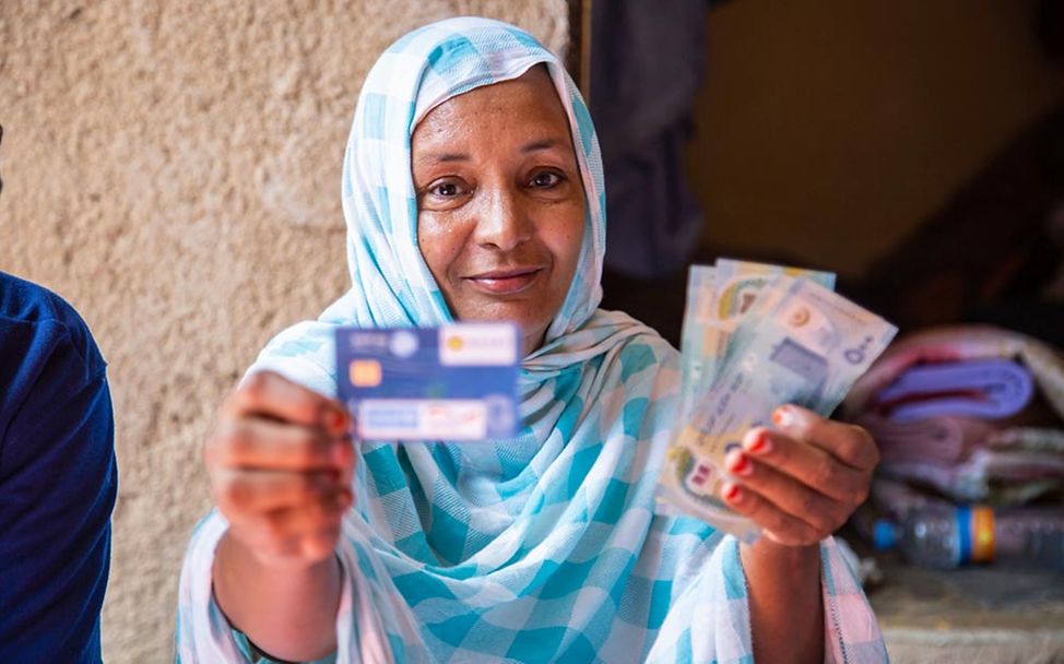 Bargeldhilfe (cash transfer): Eine Frau in Mauretanien hält ihre Bankkarte in der einen, Geldscheine in der anderen Hand. 