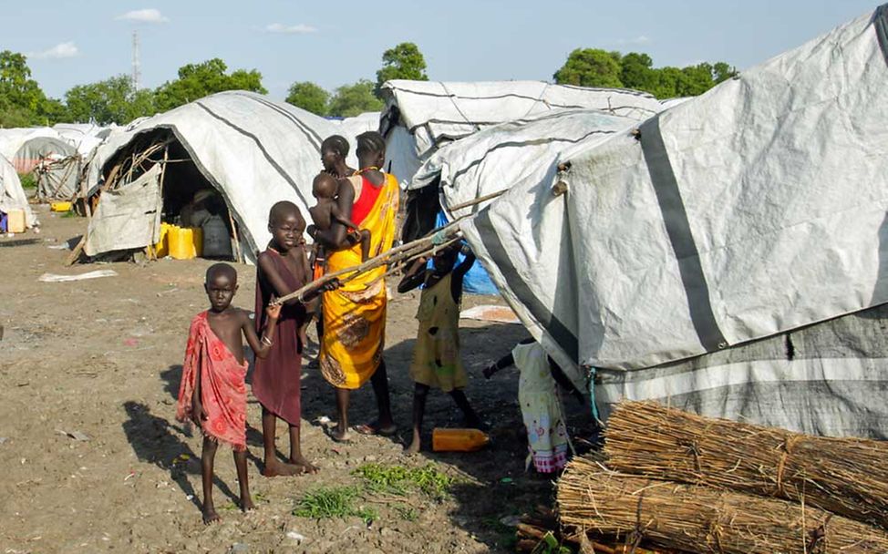 Nothilfe Südsudan: Eine Familie steht in einem Flüchtlingslager unter einer Zeltplane. 