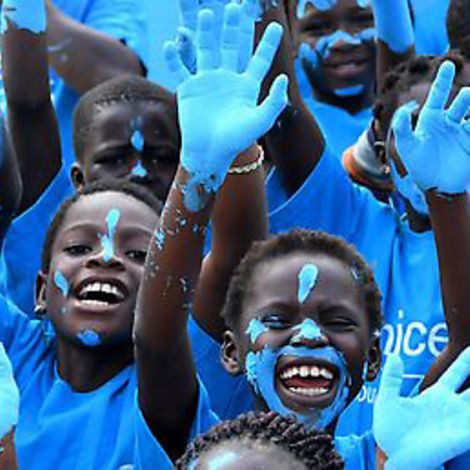 Strahlende Kinder aus der Elfenbeinküste halten ihre blau bemalten Hände in die Luft.