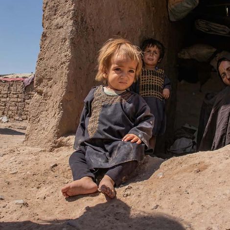 Afghanistan: Ein Kind sitzt in einem Vertriebenenlager vor einer Lehmhütte