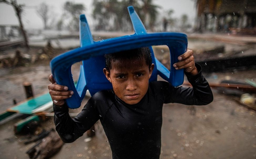 Klimaschutz spenden: Ein Junge in Nicaragua schützt sich mit einem Plastikstuhl vor Starkregen