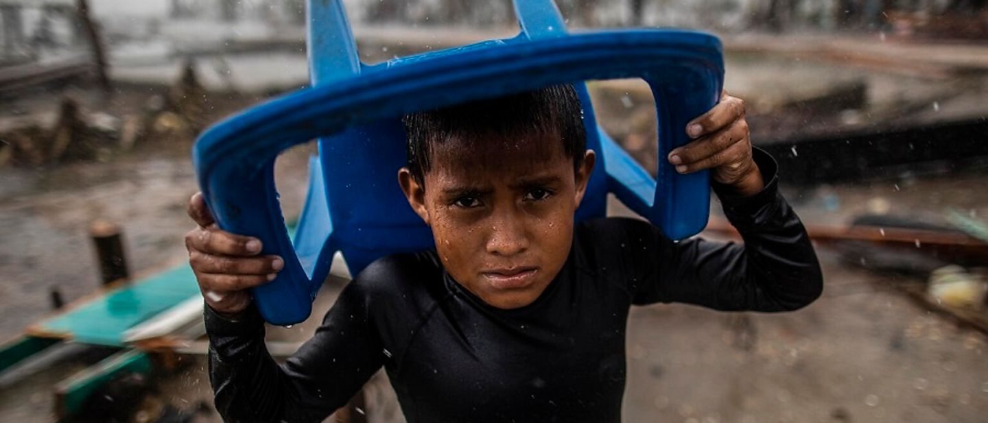 Klimaschutz spenden: Ein Junge in Nicaragua schützt sich mit einem Plastikstuhl vor Starkregen