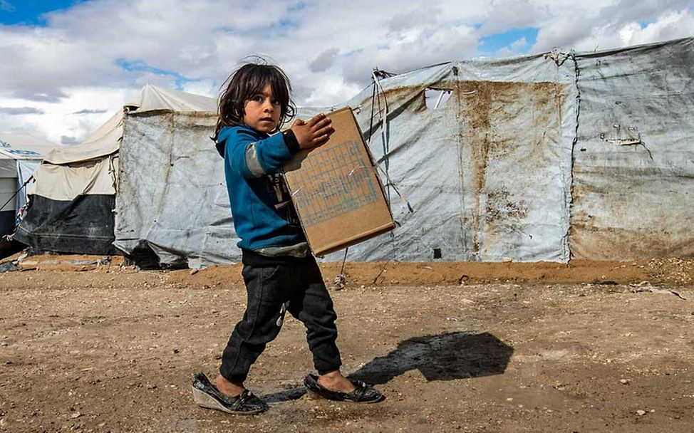 Spenden für Syrien: Ein Mädchen in einem Flüchtlingslager trägt eine Kiste mit UNICEF-Kleidung. 