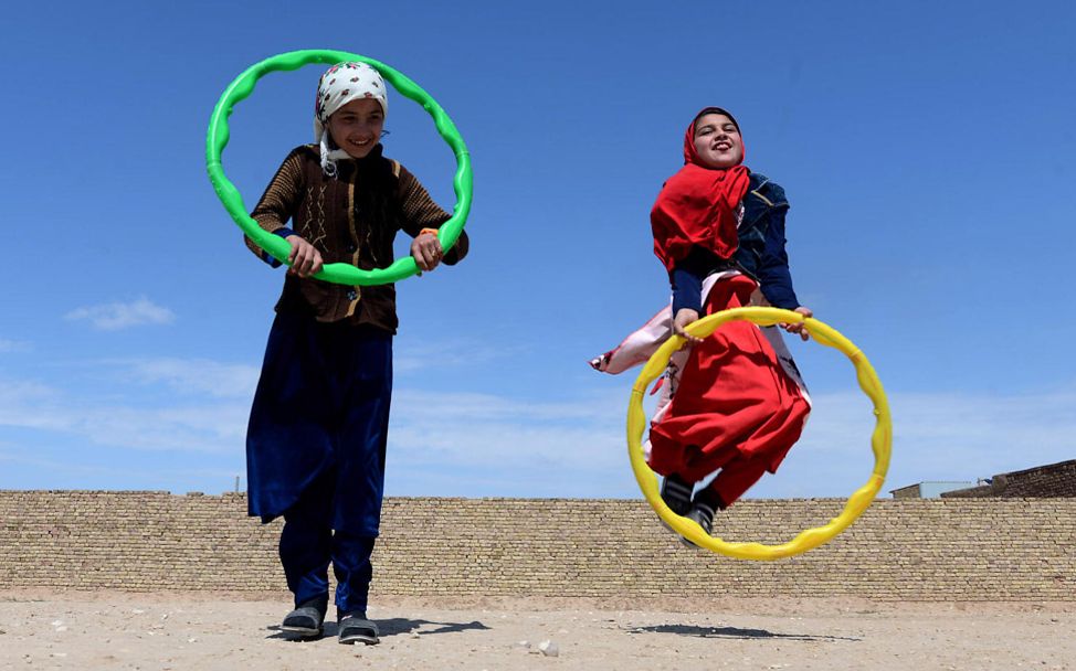 Afghanistan Kinder: Mädchen hüpfen unter blauem Himmel durch Reifen
