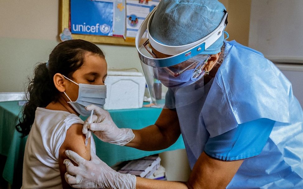 Venezuela: Mädchen wird von Gesundheitshelferin in den Oberarm geimpft.