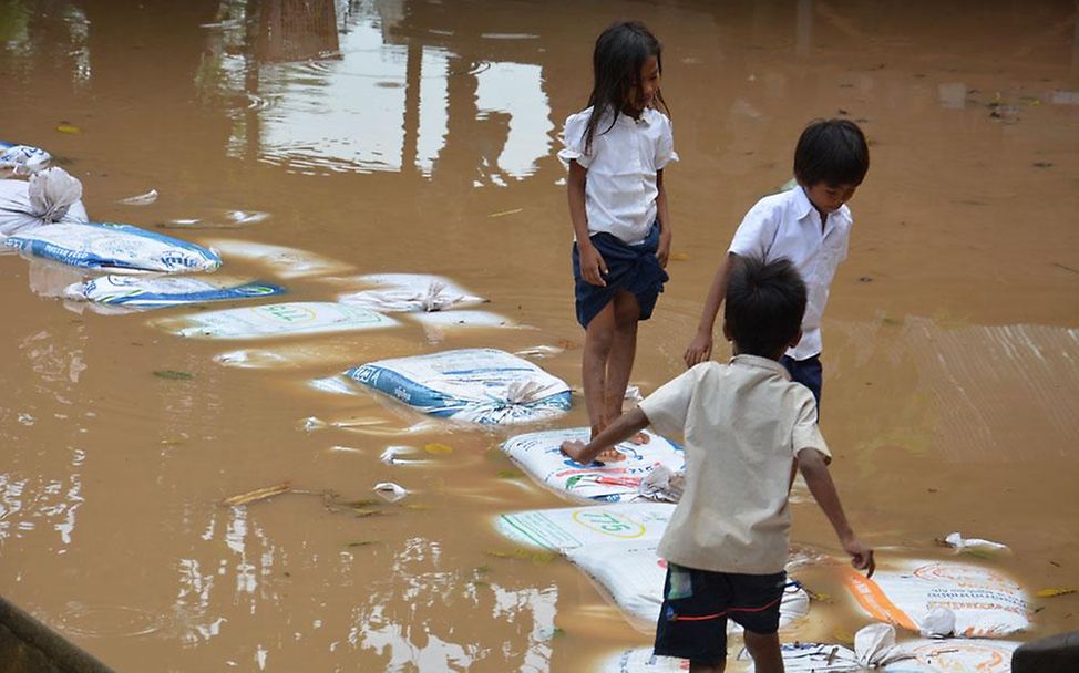 Kambodscha: Kinder balancieren auf Sandsäcken durch das Wasser