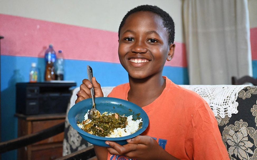 Elfenbeinküste: Ein Junge zeigt sein Lieblingsessen: Reis mit einer Sauce aus Kartoffelblättern