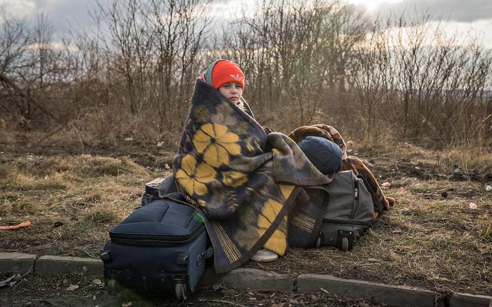 Ukraine-Konflikt: Eingehüllt in eine Decke sitzt ein geflüchtetes Mädchen auf Koffern. 