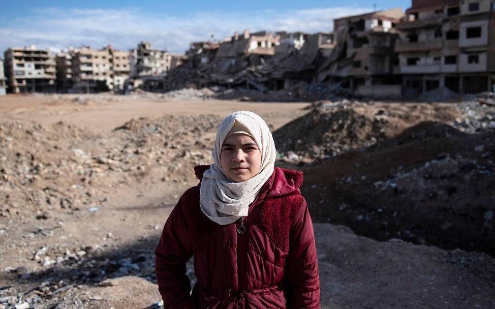 Syrien: Das Mädchen Aminah steht vor zerstörten Häusern und Trümmern.