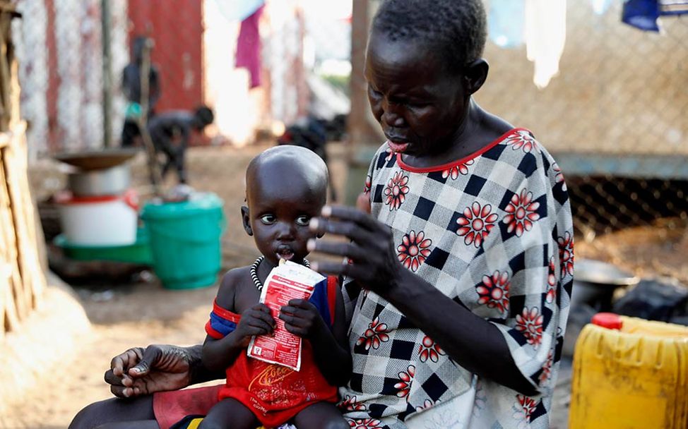 Hunger in Afrika: Ein mangelernährtes Kleinkind hält auf dem Schoß seiner Oma ein Päckchen Erdnusspaste in der Hand.