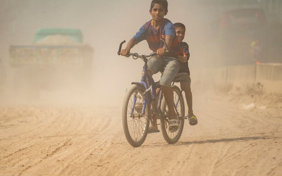 Kinder fahren Fahrrad auf einer stark verschmutzten Straße in Dhaka, Bangladesch.