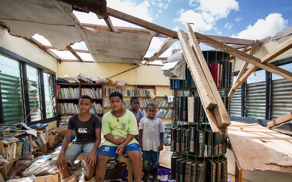 Vier Kinder stehen in der zerstörten Bücherei ihrer Schule.