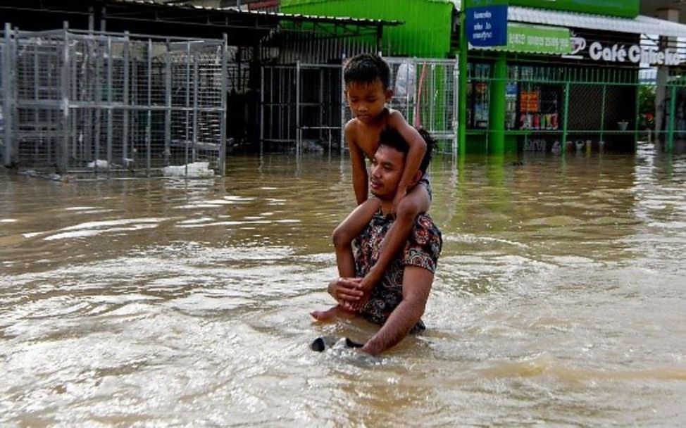 Ein Mann und sein Sohn durchwaten eine überflutete Straße am Rande von Phnom Penh in Kambodscha