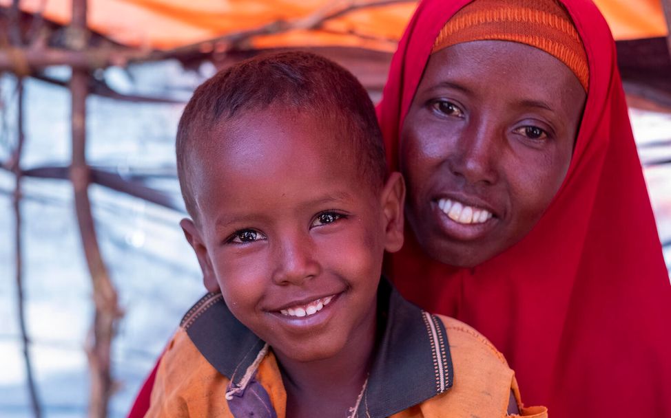 Der vierjährige Abdirahman sitzt mit seiner Mutter vor einem Zelt in einem Camp für vertriebene Familien