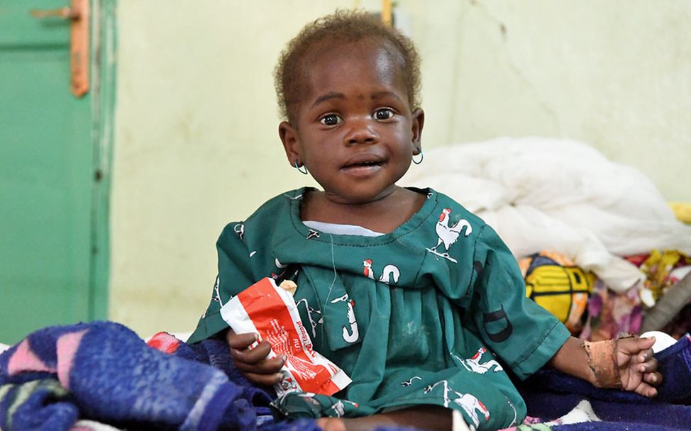 Hunger in der Welt: Ein mangelernährtes Baby im Tschad hält eine Packung Erdnusspaste in der Hand. 