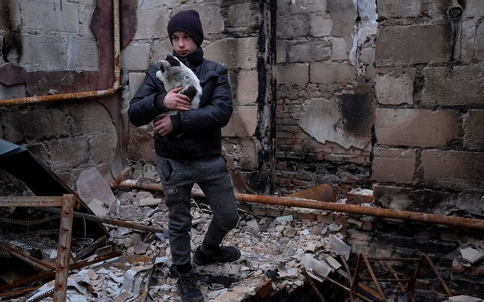 Ukraine: Junge steht mit Katze auf dem Arm in den Trümmern eines Hauses