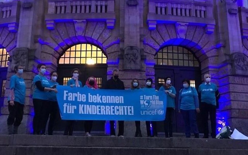 Freiburg: UNICEF engagierte halten ein Plakat zum Tag der Kinderrechte vor dem blau erleuchteten Theater hoch.