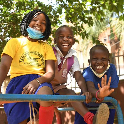 Uganda: Drei Kinder lachen auf einem Schulhof.