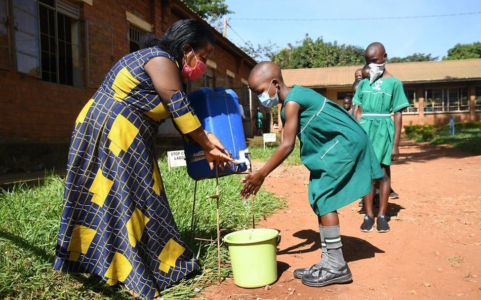 Uganda: Eine Lehrerin hilft einer Schülerin beim Händewaschen.