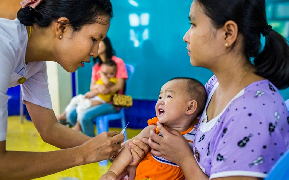 Myanmar: Kind sitzt im Schoß seiner Mutter und wird geimpft.