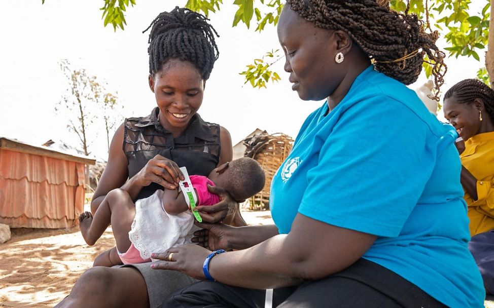 UNICEF-Ernährungsspezialistin im Südsudan, zeigt Mutter wie das Maßband richtig anlegt wird.