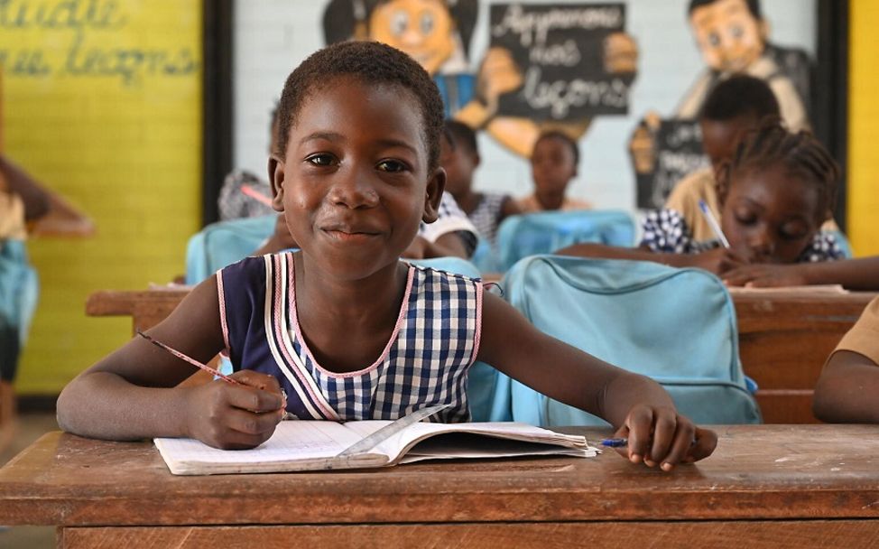 Elfenbeinküste: Mädchen sitzt mit Buch an ihrem Schultisch.