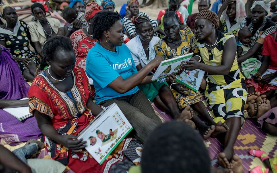 UNICEF-Mitarbeiterin zeigt Müttern ein Schaubild zu gesunder Ernährung.