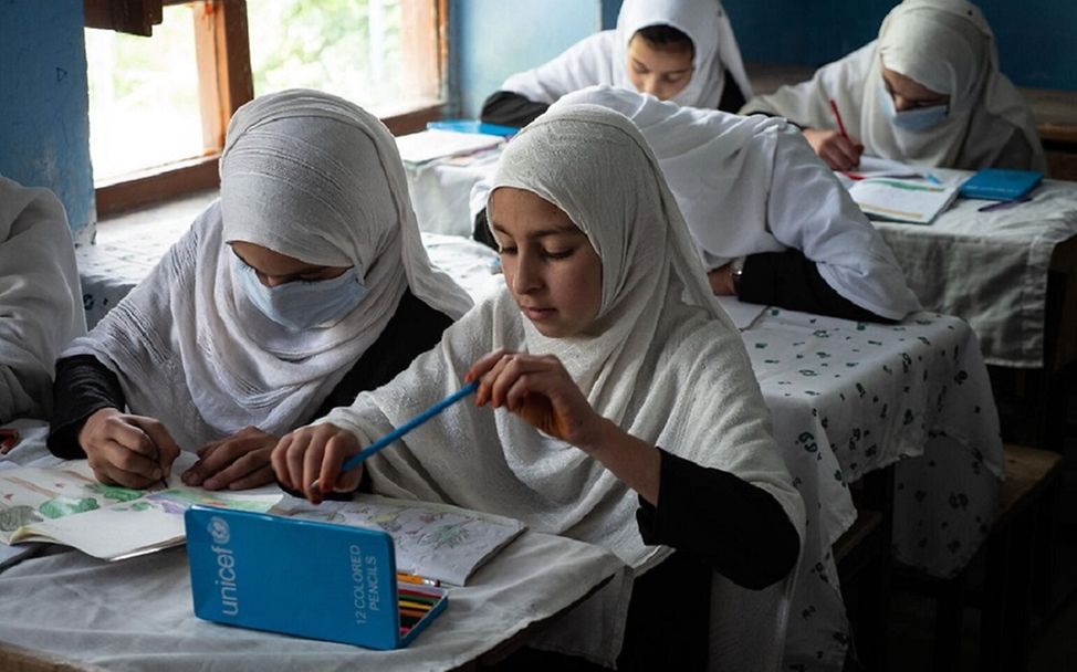 Afghanistan: Zwei Mädchen sitzen mit Schulmaterial an einem Tisch.