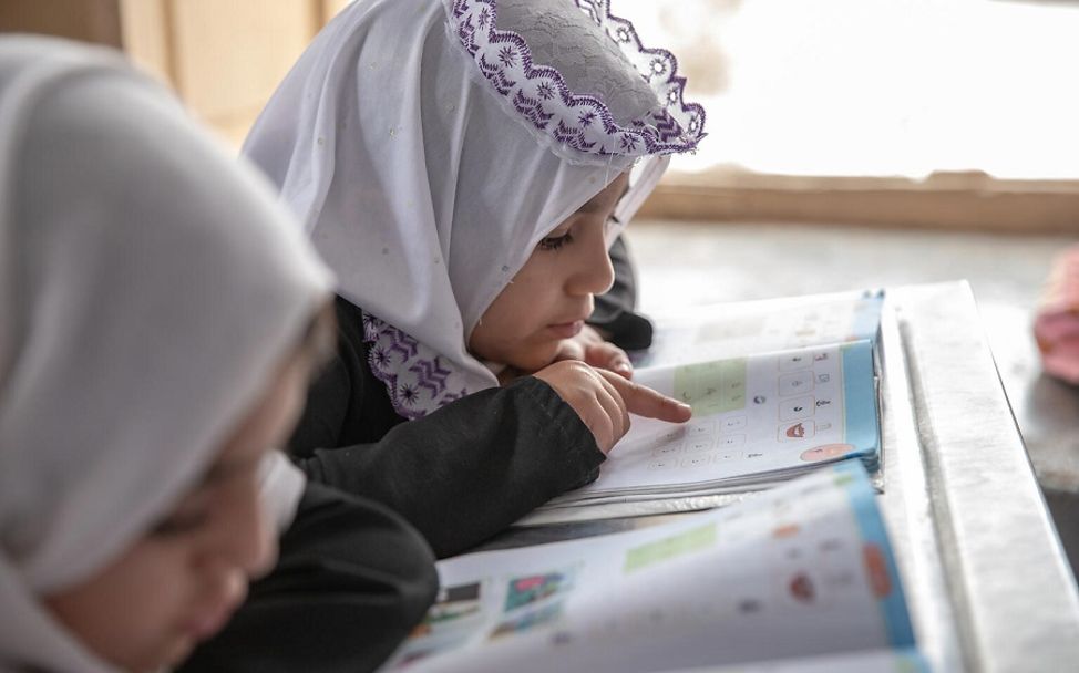 Afghanistan: Zwei Mädchen schauen auf ein Lernbuch.