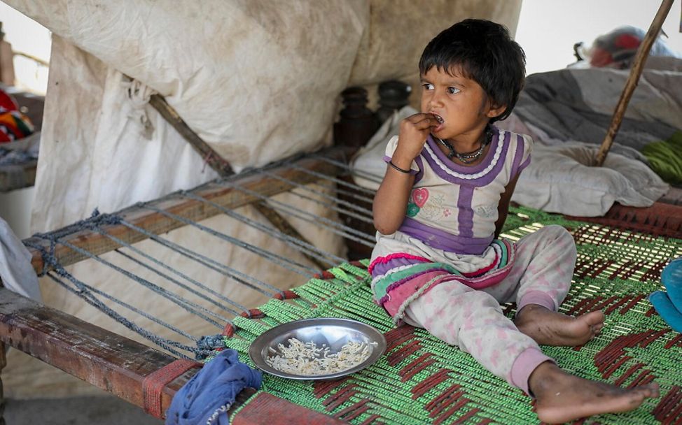 Pakistan: Mädchen sitzt in einer Notunterkunft uns isst Reis.