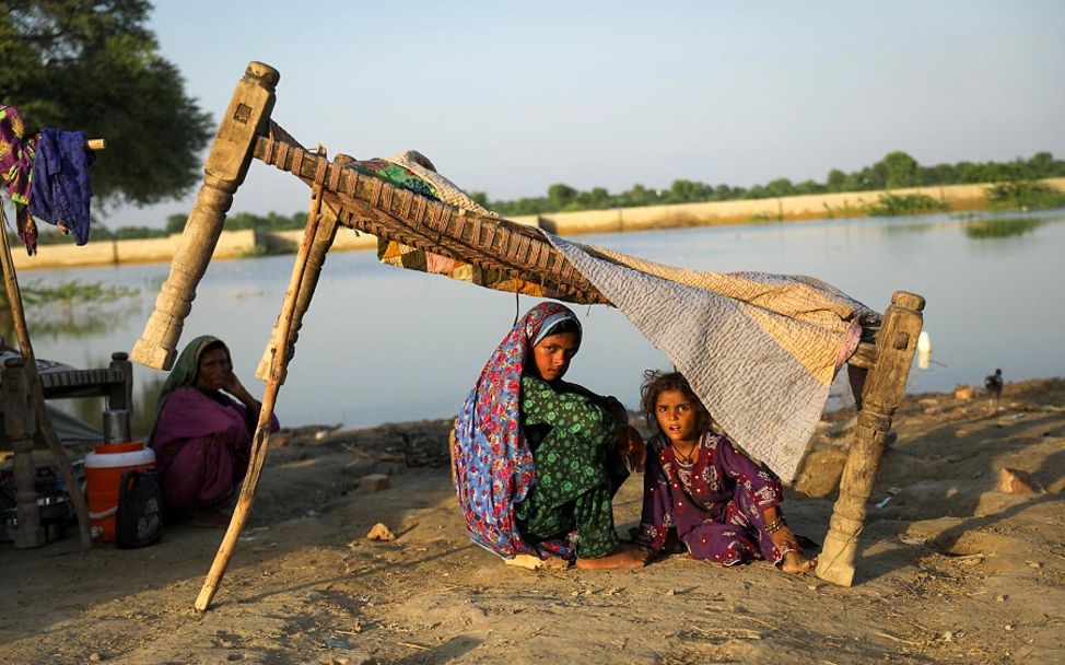 Flut Pakistan: Mutter sitzt mit Kinder unter behelfsmäßigem Zelt.