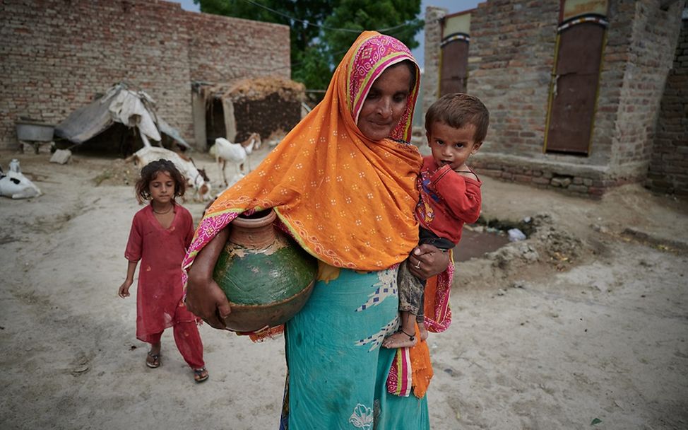 Pakistan: Eine Mutter hält unter dem linken Arm einen Wasserkrug und auf dem rechten Arm ihren Sohn.