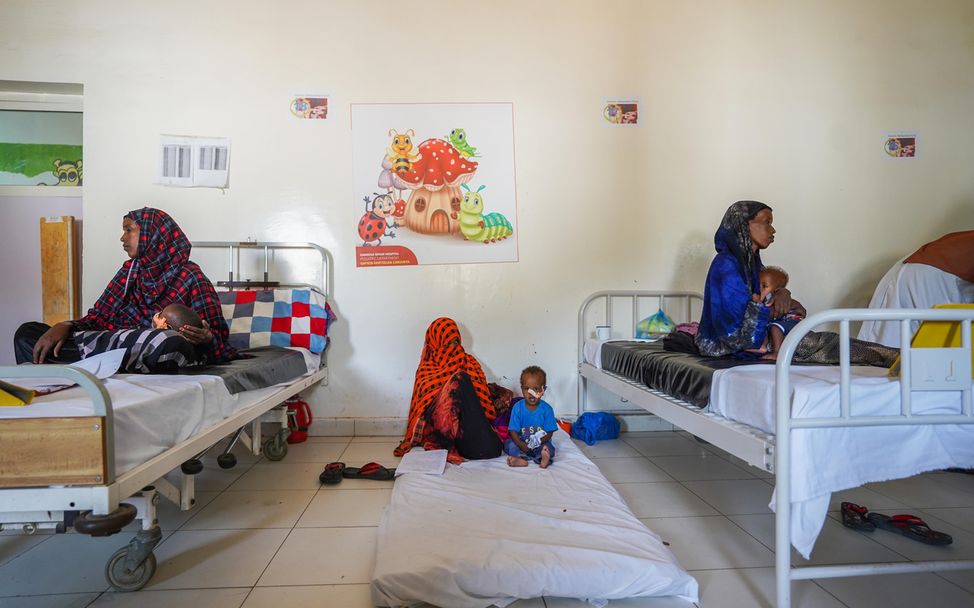 Mütter sitzen mit ihren Kindern auf Matrazen in Betten und auf dem Boden in einem Krankenhaus.
