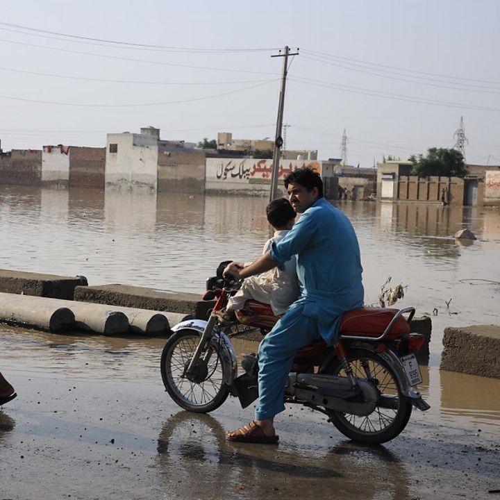 Pakistan: Ein Mann fährt mit einem kleinen Kind auf einem Motorrad durch die überschwemmten Gebiete.