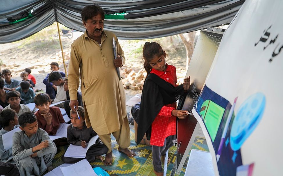 Pakistan: Ein Mädchen zeichnet etwas an eine provisorischen Tafel in einem Zelt.
