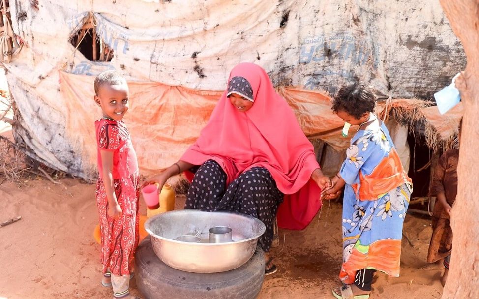 Somalia: Eine Frau mit zwei Kindern vor einer Schüssel mit Wasser.