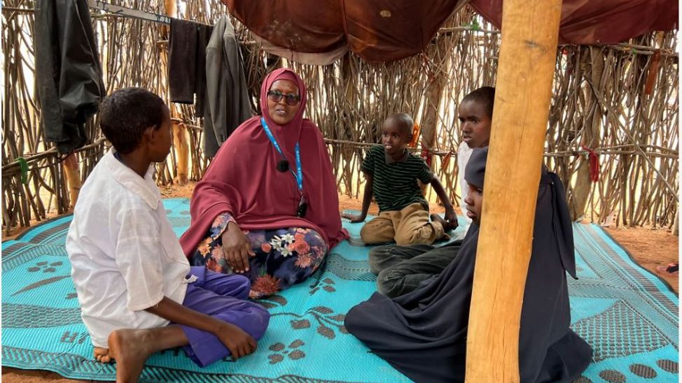 Kenia: Kinder sitzen mit UNICEF-Kinderschutzexpertin zusammen und unterhalten sich.