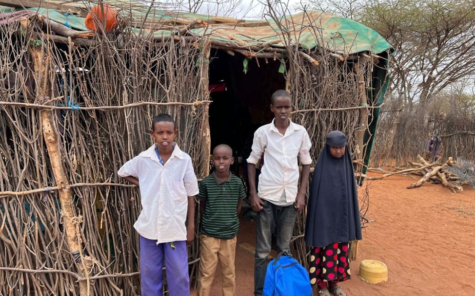 Kenia: Junge steht mit Geschwistern vor Hütte, die ihr Zuhause ist.