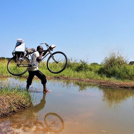 Demokratische Republik Kongo: Ein Helfer trägt Hilfsgüter auf einem Fahrrad über einen Fluss.