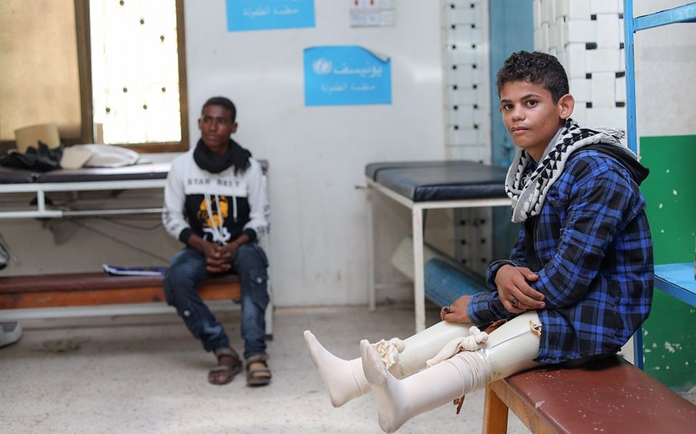 Ein Junge mit Beinprothesen sitzt auf einer Bank in einem Prothesenzentrum.